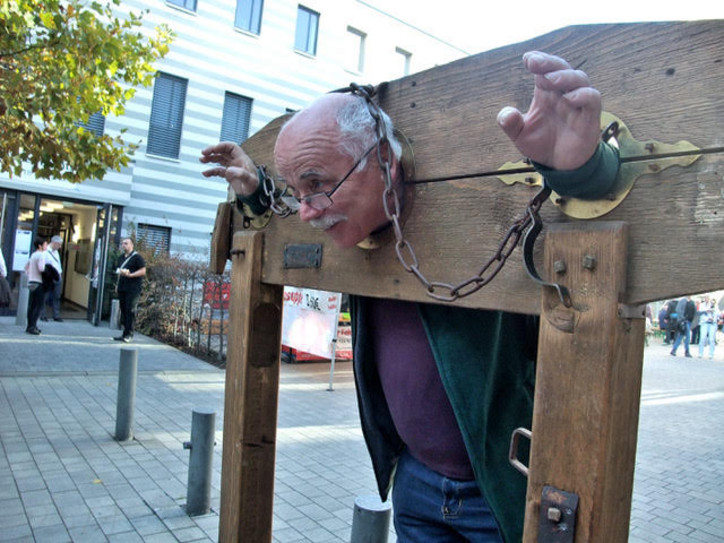 Ein Mann eingespannt in einem altertümlichen Pranger als Fotomotiv